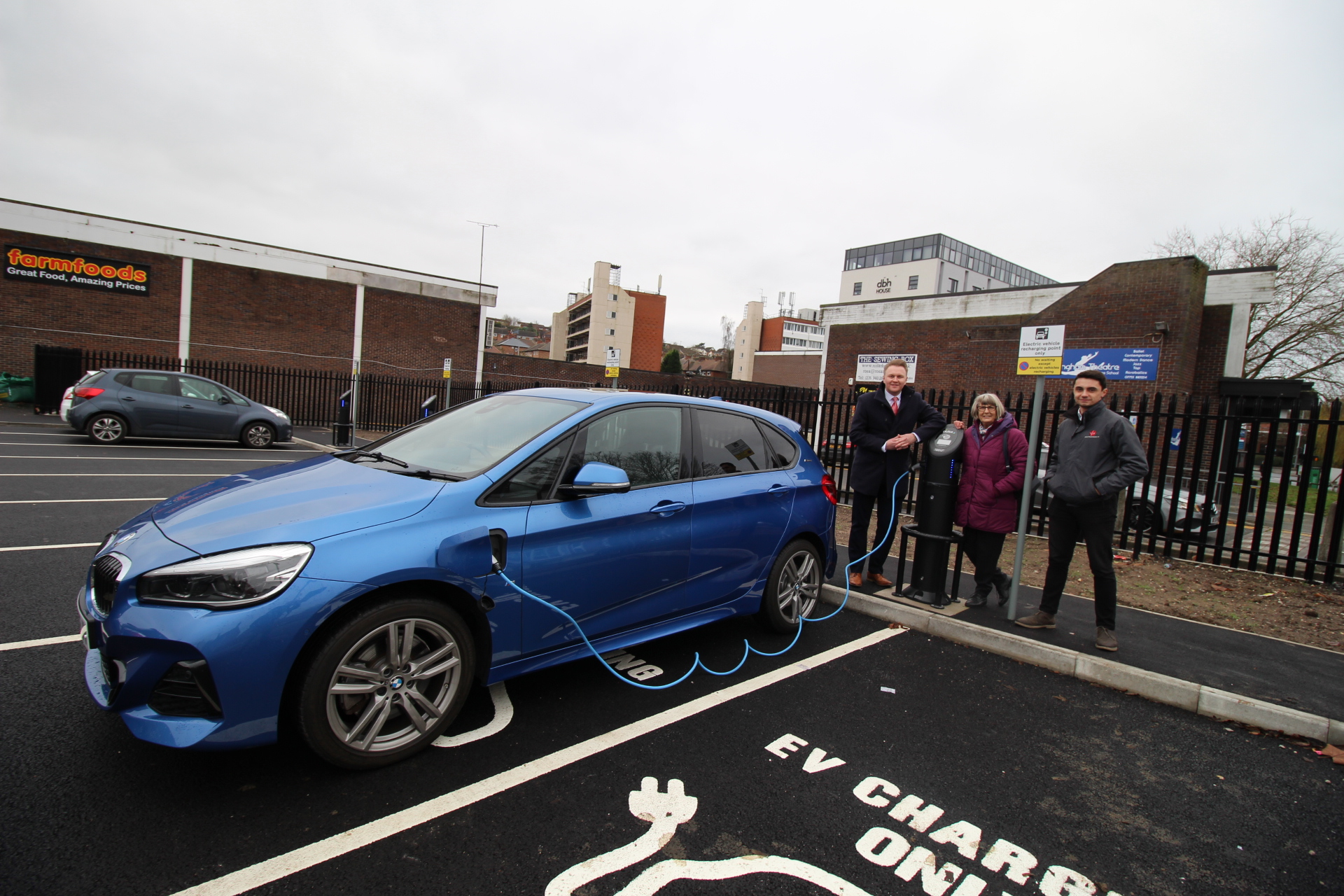 A blue hybrid car parked in an Electic Charge Point with Councillor Michael Payne, Councillor Jenny Hollingsworth and representative from MG LTD