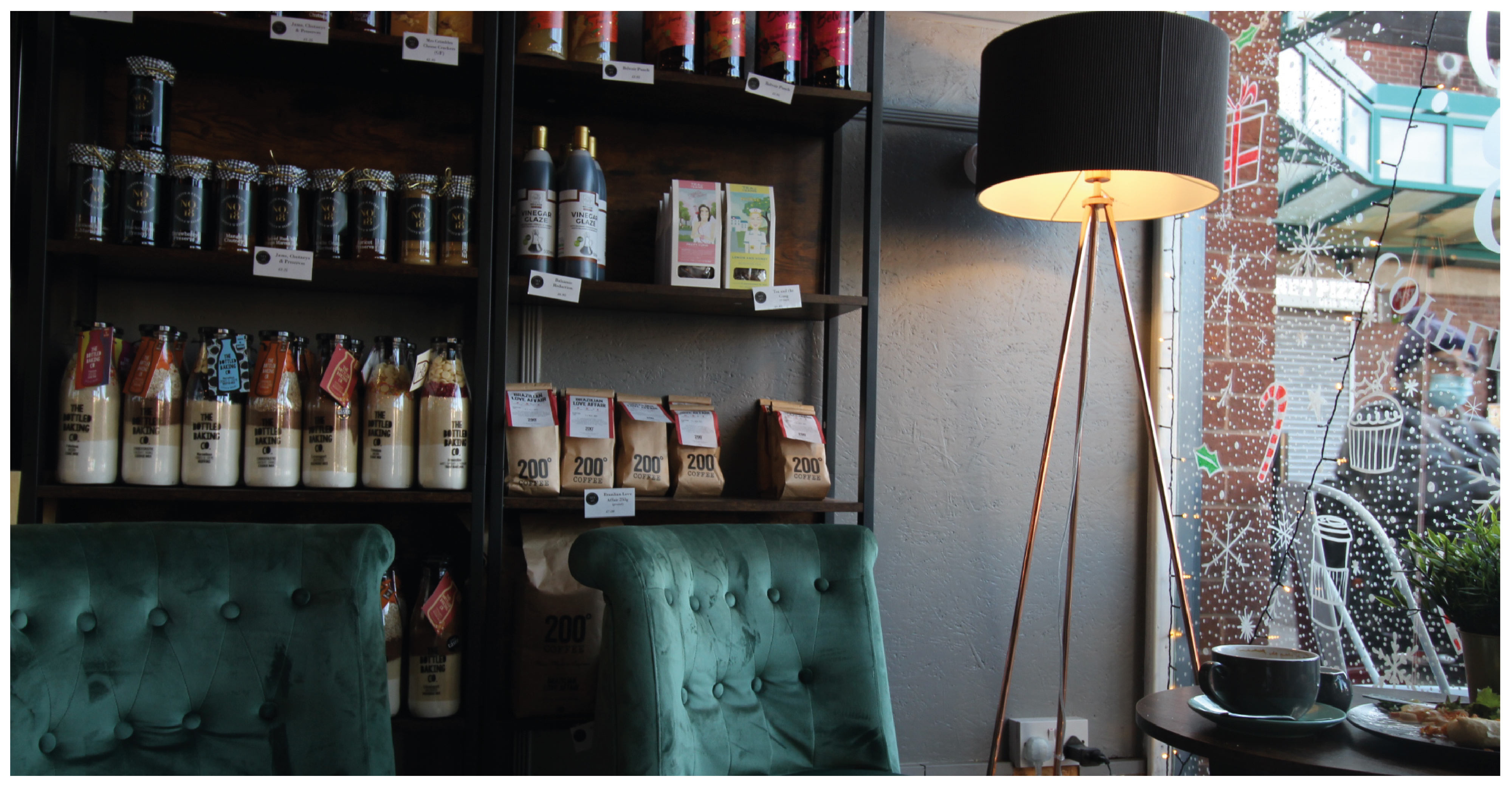 the inside of a coffee shop with two dark green chairs and coffee bags behind them on shelves