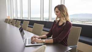 A woman sat at a large empty desk on a laptop