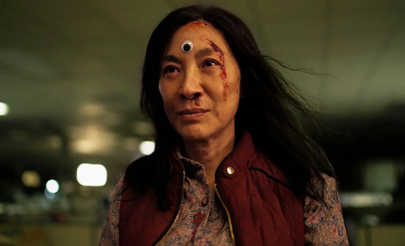Actress Michelle Yeoh stands with a googly eye in the middle of her forehead and blood coming down one side of her face